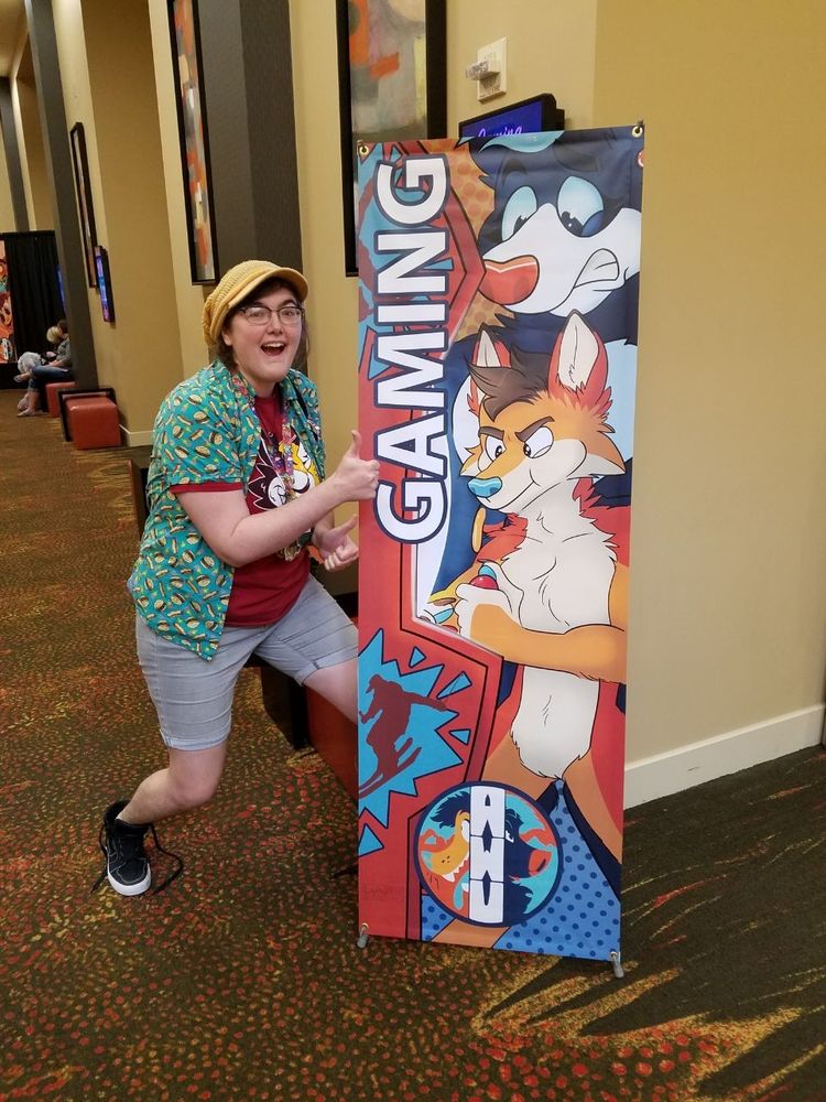Photo of Luna giving a enthusiastic thumbs-up to their AWU vinyl 'Gaming' banner.

Arc (anthro coyote) is intently focused on an arcade cabinet video game. Carver (anthro bear) stands behind Arc grimacing.