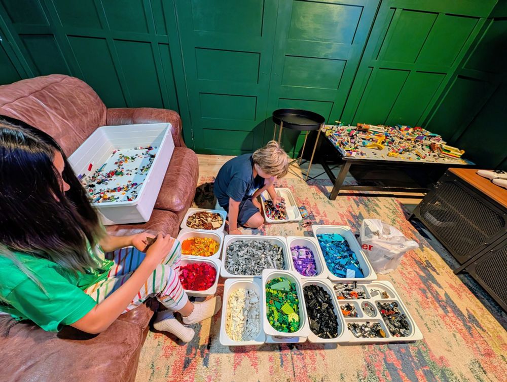 Lego sorting, bins for different colors. Two kids sorting Legos, one on the couch, one on the floor. 