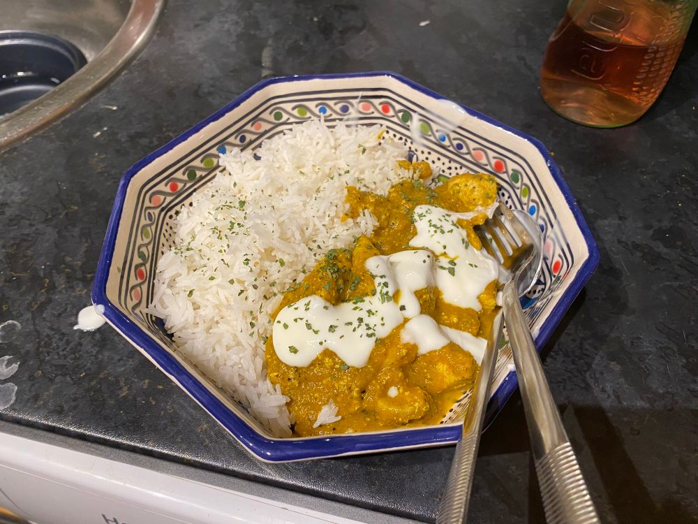 A bowl of curry and white rice, topped with yoghurt and coriander 