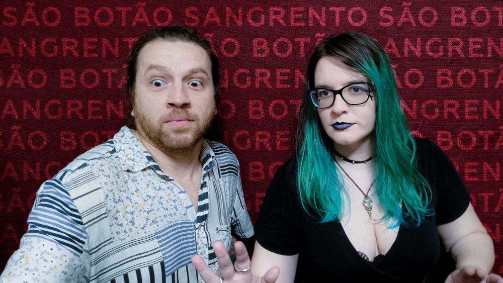 Aran e Thais, lado a lado. Aran está à esquerda, com os olhos esbugalhados olhando para algo no chão, tal qual uma barata gigante... Ele usa uma camisa branca com listras e pequenas florezinhas. Thais está à direita, com as mãos na frente do corpo, como quem vai proteger Aran de algo. Ela olha séria, ams preocupada, para algo além da câmera. Ela veste uma camiseta preta e um colar com um pingente metálico.

Atrás, o fundo é vermelho e tem em transparência escrito as palavras SÃO BOTÃO SANGRENTO diversas vezes...
