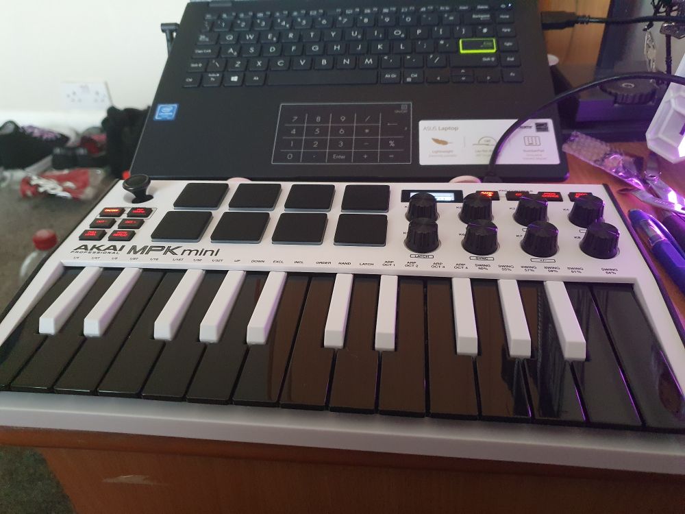 A white synthesiser with black keys sat in front of a black laptop resting on a hidden support.