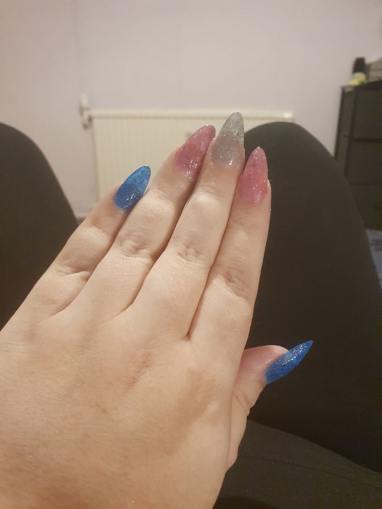 Nails painted in blue pink and white glitter effect to create the trans flag.