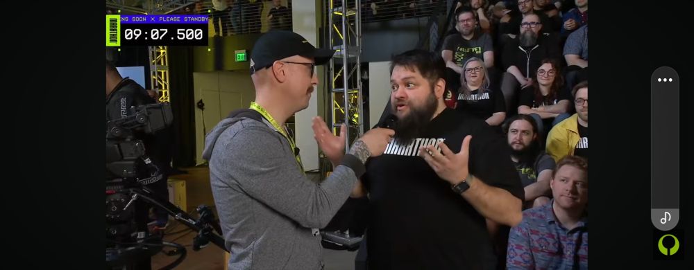 Super awesome designer Kevin Yanes talks about Marsthon. He has a beard and black shirt, and is being interviewed via microphone by another man in a grey hoodie and dark baseball cap. 