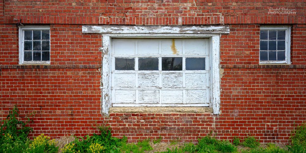 A brick industrial building with a loading dock garage door and a window on each side of the door.