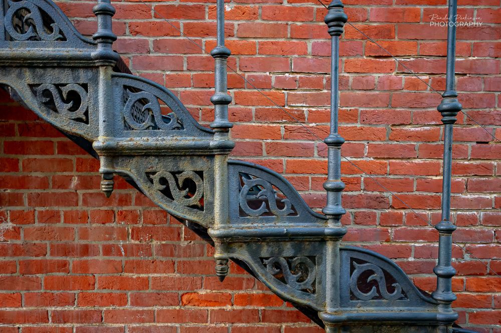 Closeup of ornate cast iron stairs from the 19th Century adjacent to a red brick wall.