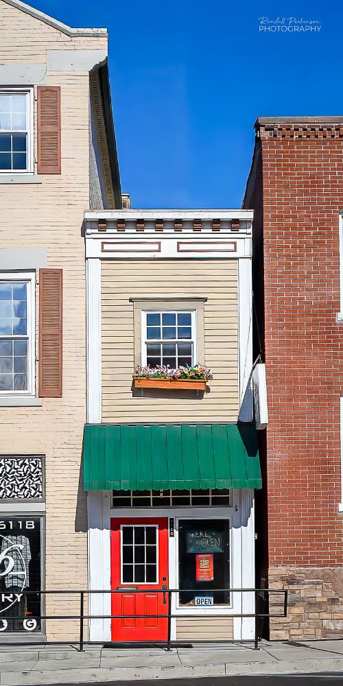 A narrow two-story building only about 10 feet wide sits between two taller adjacent buildings.