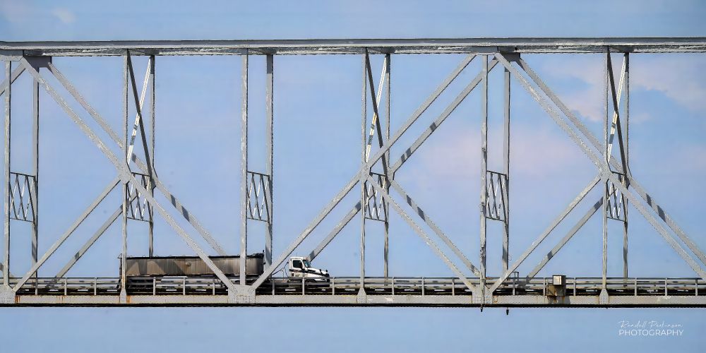 A truck drives across a portion of a very large steel truss bridge.