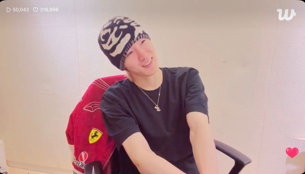 p1harmony soul during a weverse live. he’s sitting on a. rolling chair with a red ferrari jacket hanging on the back. he’s wearing a black tee and a black beanie with white graphics on it 