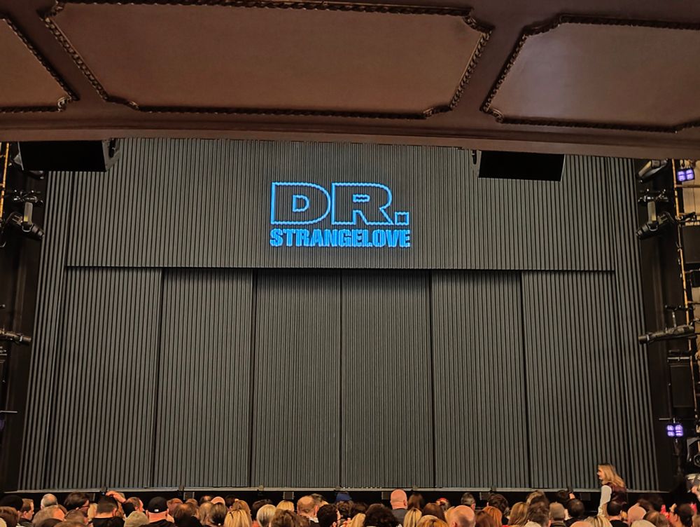 Corrugated steel shutters + khaki in colour - covering the stage at the Noel Coward Theatre on the West End of London. An illuminated sign reads DR, STRANGELOVE