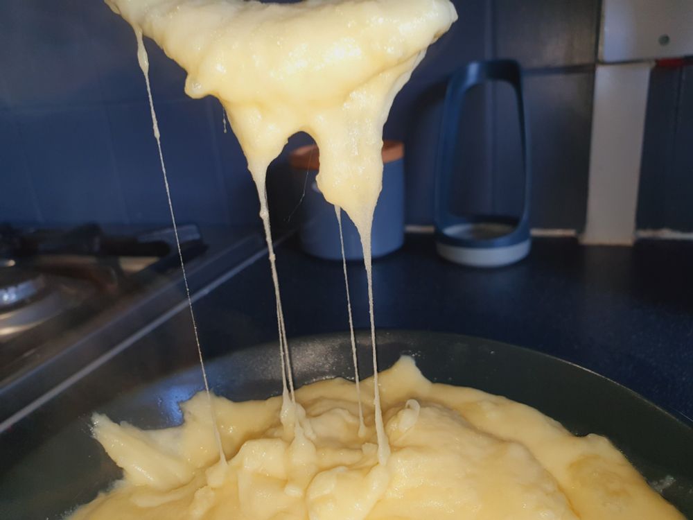 Cheesy mashed potato, you can see the cheese mixed stretch from a fork above the bowl it is served in