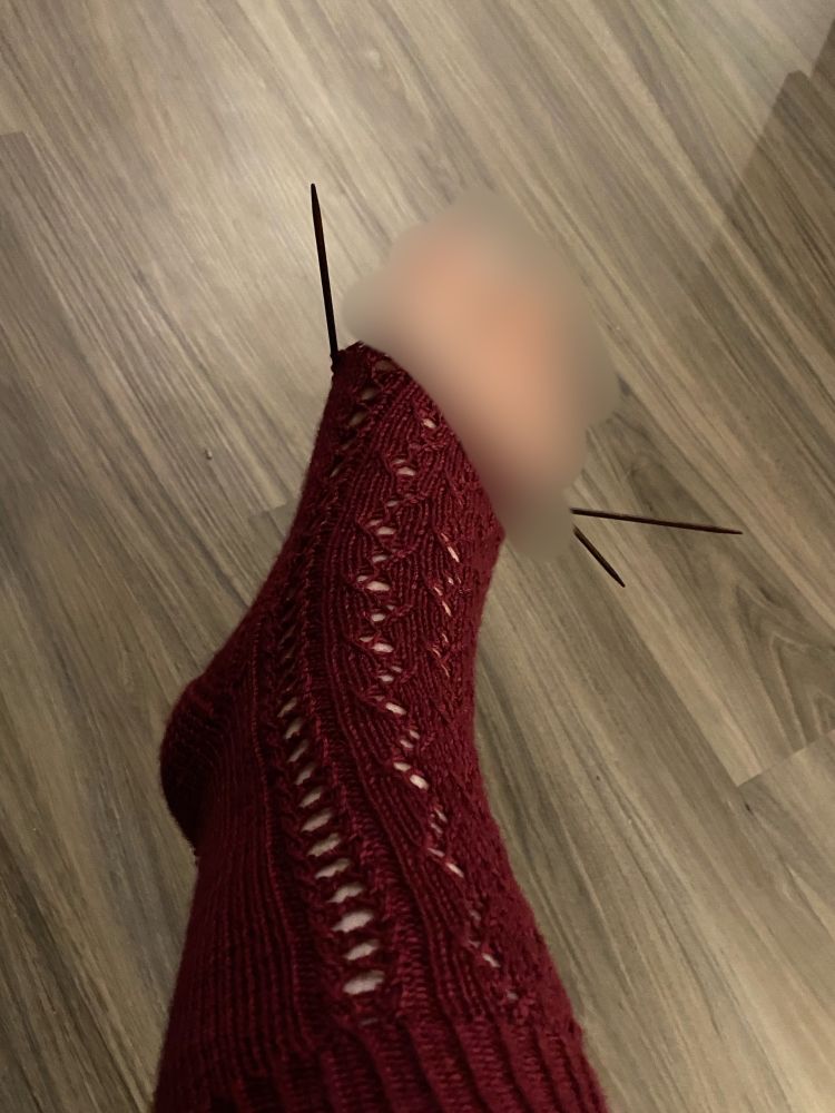 A photo of a partially complete, hand knit red sock with the toes blurred out.