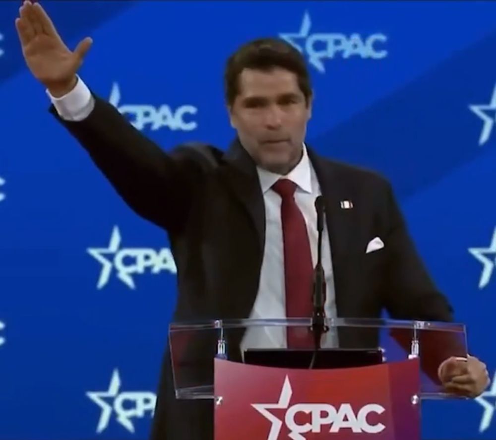 man in a suit wearing a red tie at cpac nazi salute