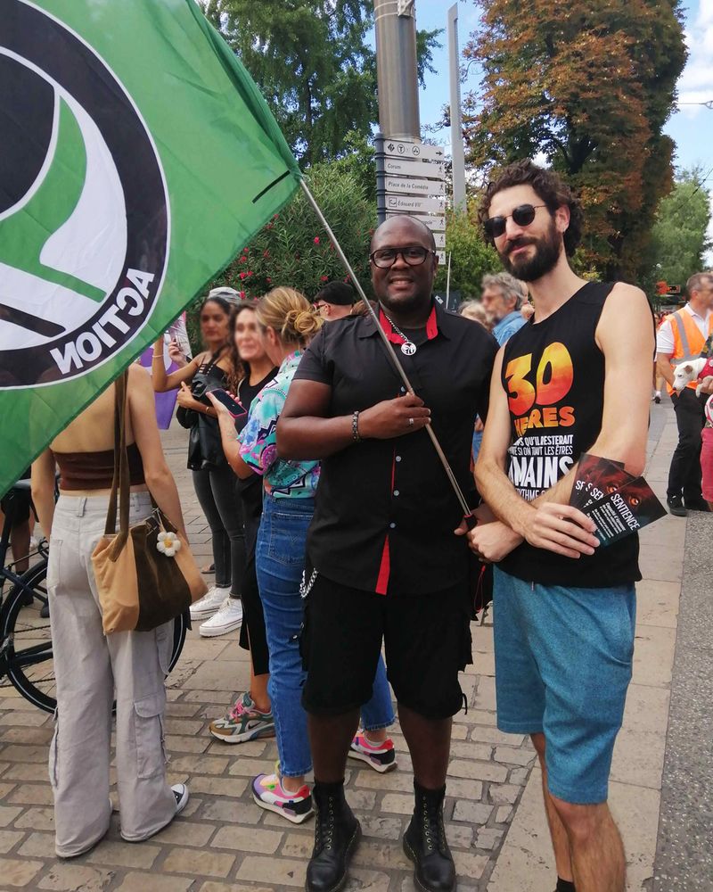 Photo de deux personnes lors de la marche. L'une porte un drapeau antispéciste & antifasciste, l'autre un t-shirt pour sensibiliser au massacre des poissons et des autocollants 