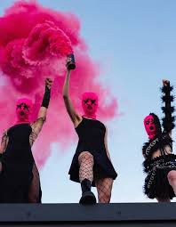 3 members of pussy riot wearing their pink balaclavas, black dresses and fish net tights. Holding their fists up in resistance 
photo: @maxavdeev