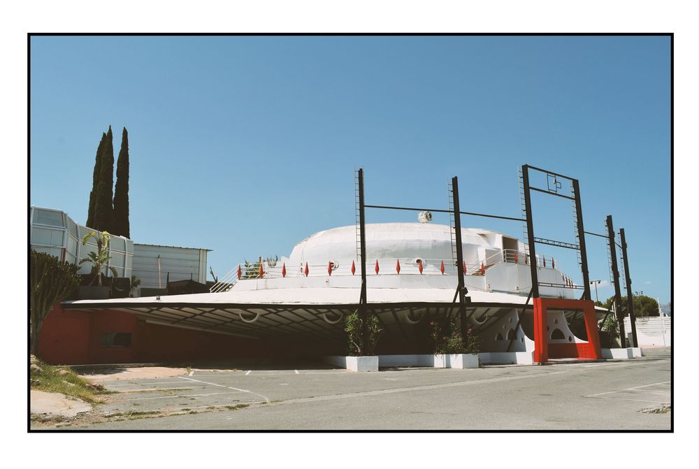 Photograph of the exterior of a spacecraft shaped nightclub. Cloudless blue sky above.