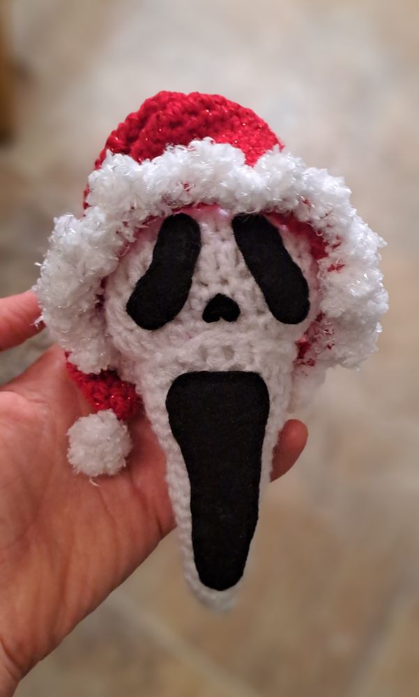 A crochet ghostface from Scream wearing santa hat