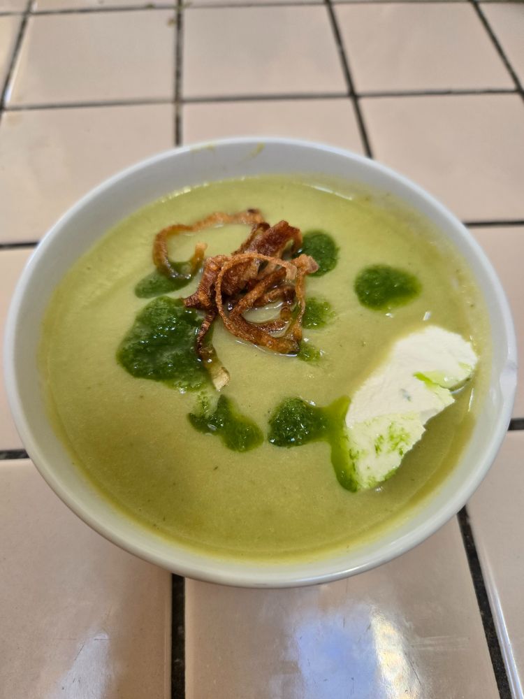 Green soup with green chive oil, brown fried shallots, and white sour cream on top.