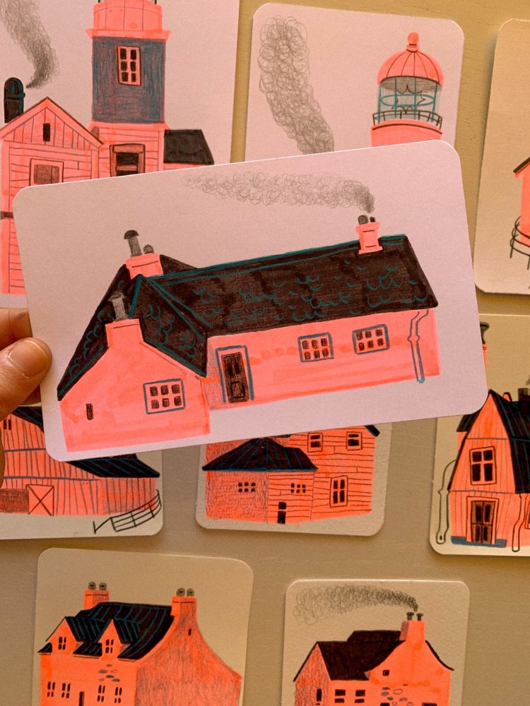 Hand holding a tiny drawing of a house, on a backdrop of other tiny drawings in the same style. The house has neon pink walls and black roof, made with markers, the details are added with black pencil for the windows, chimneys and door, and aquamarine pencil for the roof tiles, door and window frames.