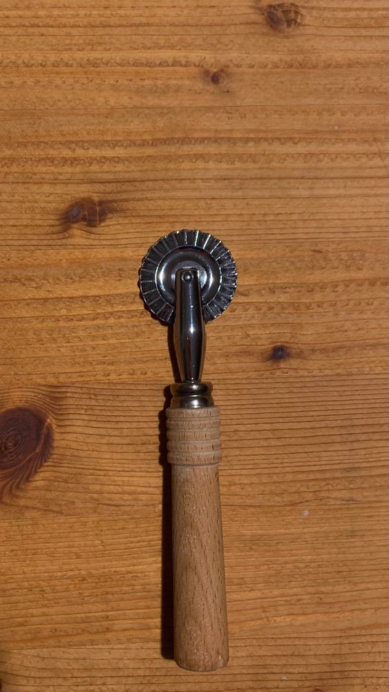 Photo of a pastry wheel cutter on a wooden kneading board.