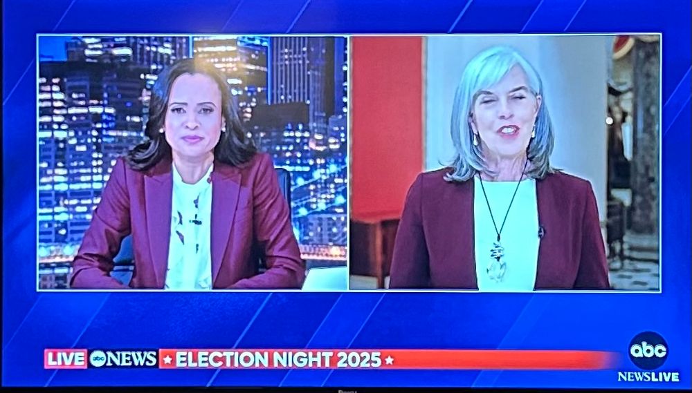 An ABC tv anchor interviews a politician on a split screen - both are wearing maroon blazers.