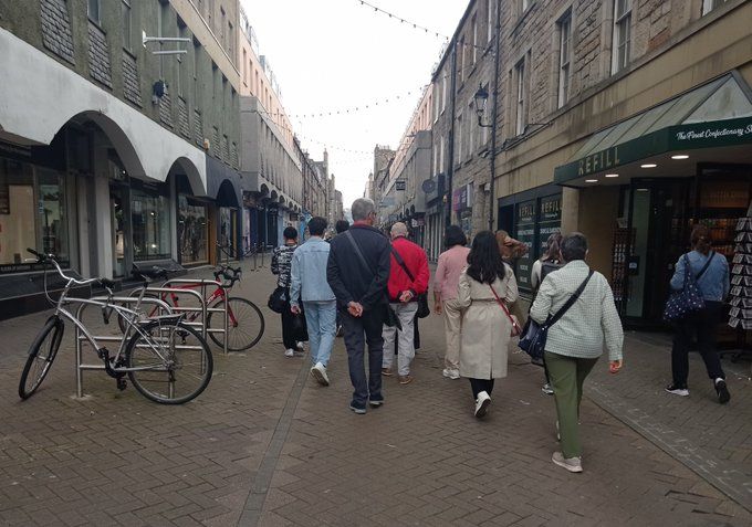Rose St Edinburgh - a narrow street in Edinburgh with paving tiles, cycle racks and a 5 wide group of pedestrians. 