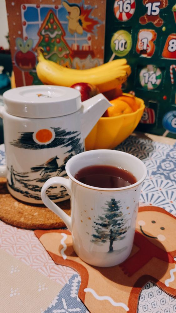 A festive cup filled with mulled "wine" with a moomin themed teapot on the background 