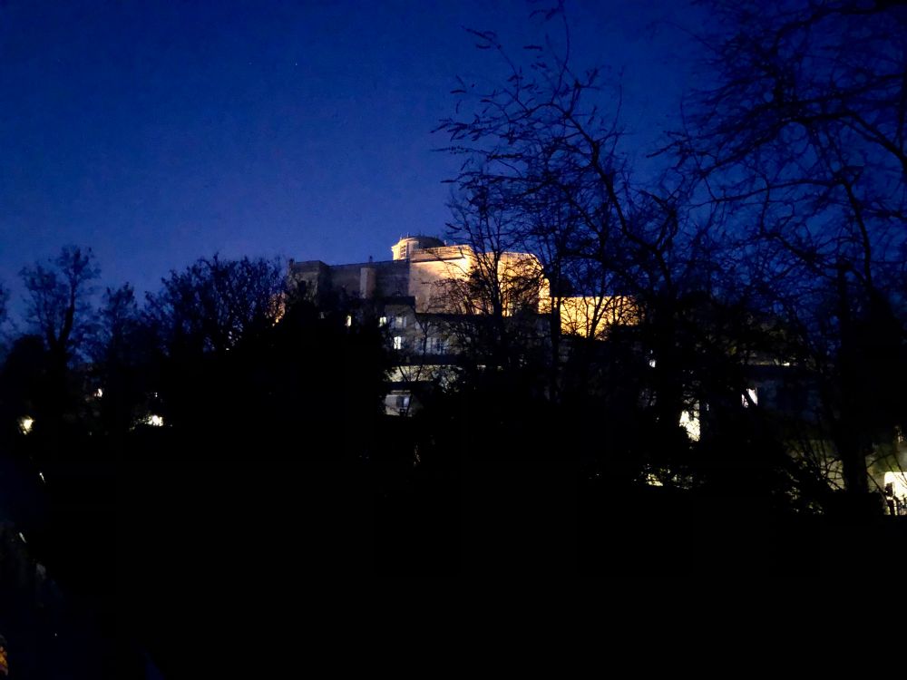 Blaue Stunde. Blick auf ein altes, erhöht liegendes Dorf. Das zentral gelegene Schloss wird angestrahlt. 