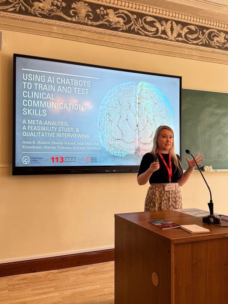 Presenter standing in front of a screen displaying a presentation titled "Using AI chatbots to train and test clinical communication skills: A meta-analysis, a feasibility study, and qualitative interviewing"