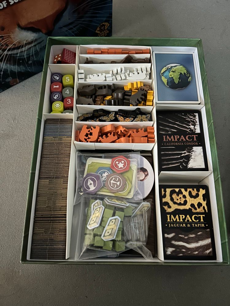 Overhead shot of Endangered with the insert.

Left bottom: All game tiles 
Left middle: Player dice
Left top: Orange and black game dice, calendar marker
Middle top: Animal tokens in two trays 
Middle bottom: Animal placards, animal boards, player boards, money, influence cubes, player mini cards and tokens
Right bottom/middle: Animal cards 
Right top: Player cards, reference cards, U.N. cards, campaign cards