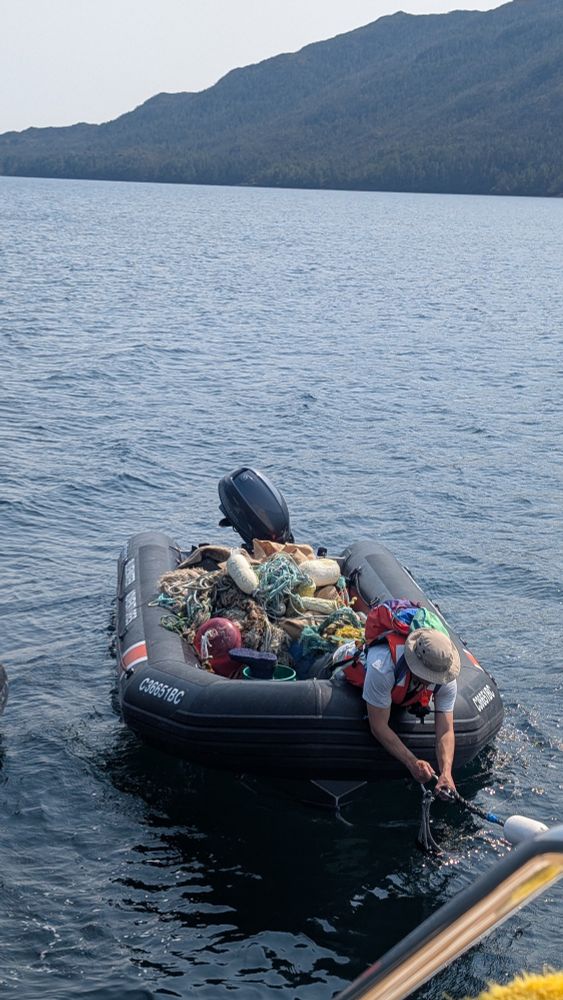 Zodiac boat full of garbage, with crew leaning over the front of the boat 