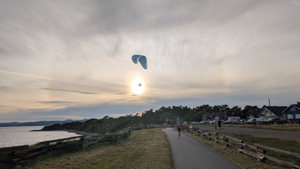 Sea on left, sun in center, paraglider wing is above the sun and paraglider is center of the sun.