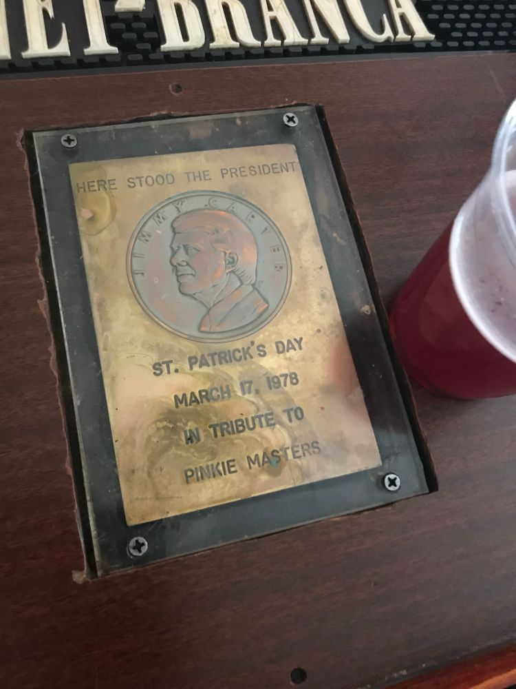 A brass plaque featuring President Jimmy Carter in profile with the text “Here stood the president. St. Patrick’s Day, March 17, 1978, in tribute to Pinkie Masters. 