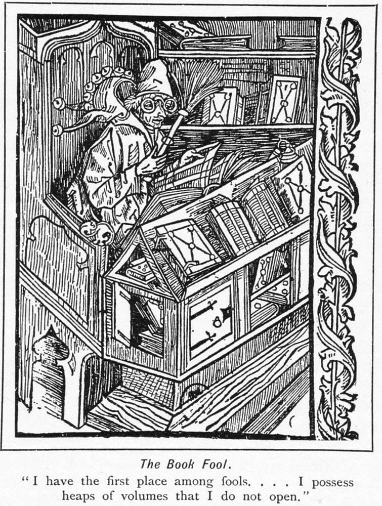 A medieval woodcut of a man in a big wooden chair. He is wearing round glasses and for some reason has a brush in his hand. He is surrounded by books. It was captioned 'The Book Fool. "I have the first place among fools... I possess heaps of volumes that I do not open".'
