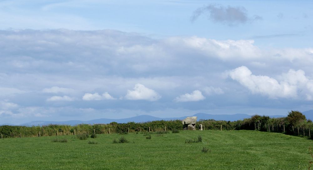The tomb can be seen in context at the far end of a field with the blue peaks of mountains in the distance.