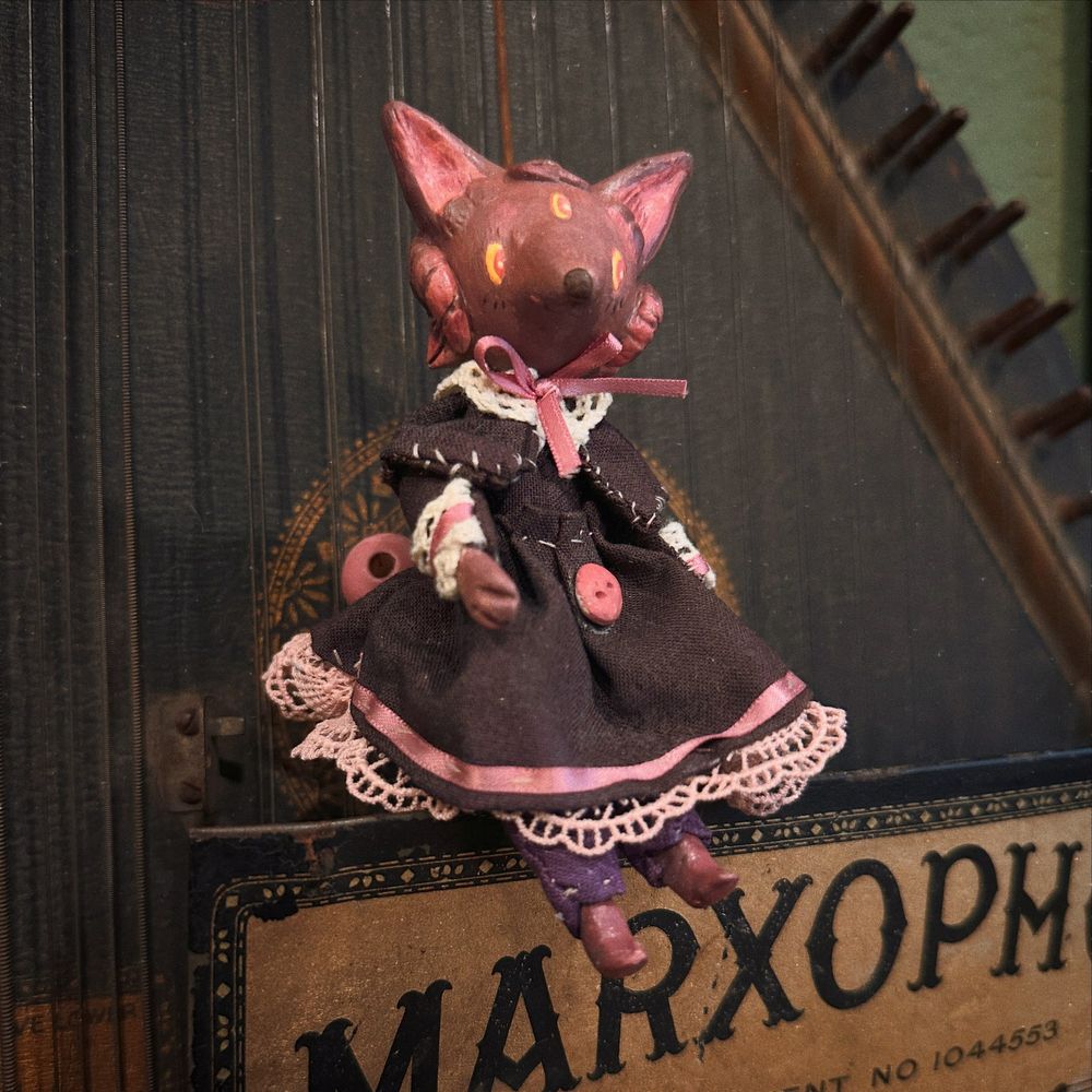 A small purple dog art doll with a simple black dress with lacy frill sitting on a Marxophone