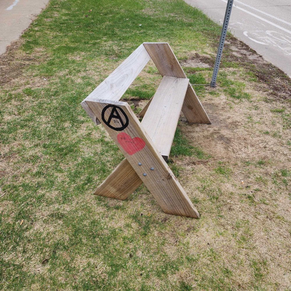 Bench at a bus stop with an anarchy symbol and a heart painted on the side 