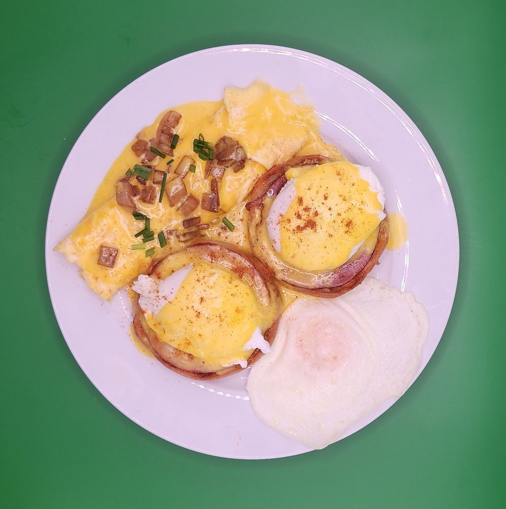 A plate with a french omelette topped with hollandaise, sauteed onions, and chives; eggs benedict; and a fried egg.