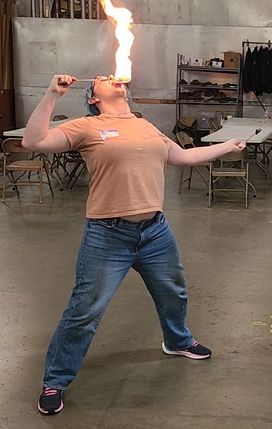 Me in an orange shirt and jeans, tipping my head back touching a lit torch to my tongue.