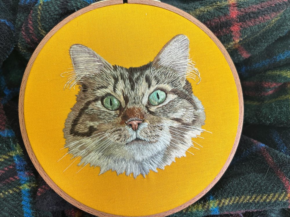 Embroidery of a long-haired brown tabby on yellow fabric 
