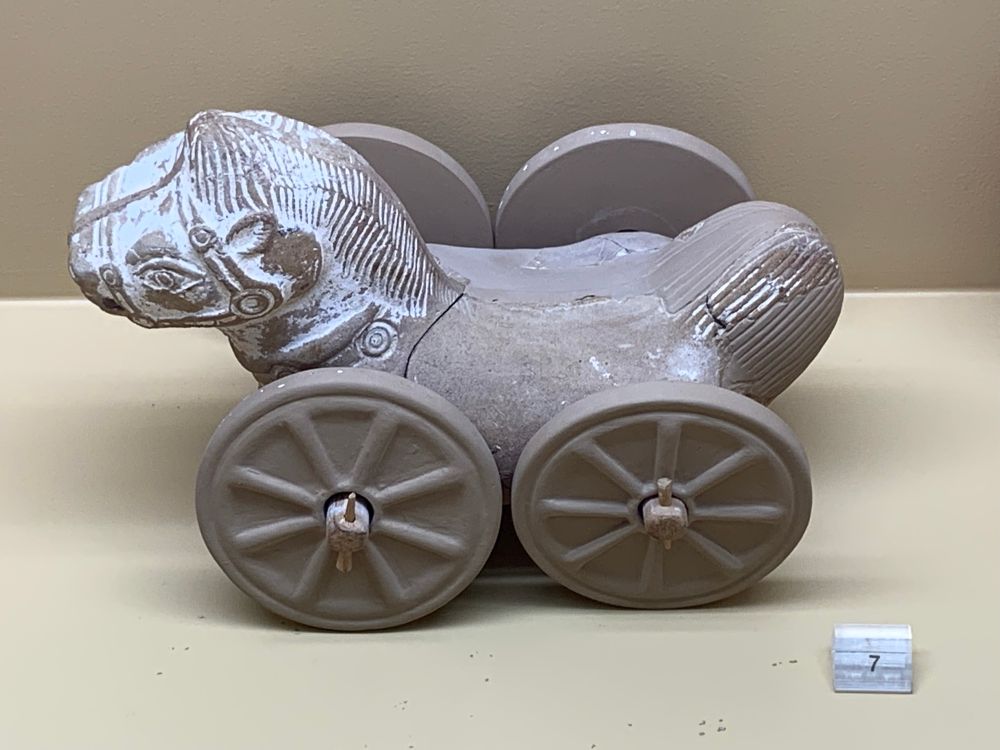 A terracotta toy horse on four wheels with stylised cute  horse head.