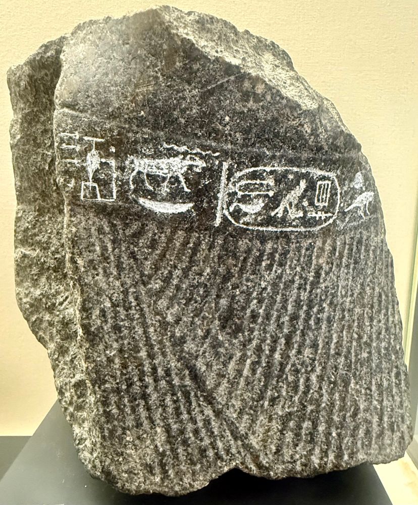 An ancient Egyptian statue fragment in salt and pepper granite: A pleated kilt, belt with hieroglyphs ‘son of ra: Psammetico, beloved of Khnun, lord of the cateract’ and lower part of belly. 