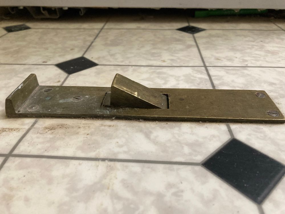 A brass doorstop on top of vinyl flooring. Side view. 