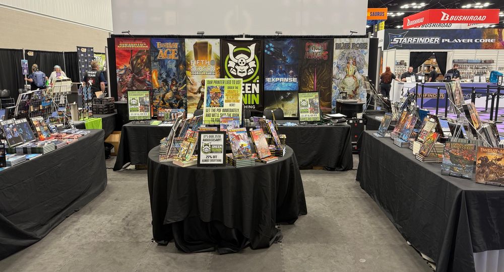 Tables stacked with RPG books and games for Green Ronin Publishing on the convention floor at Gen Con. 