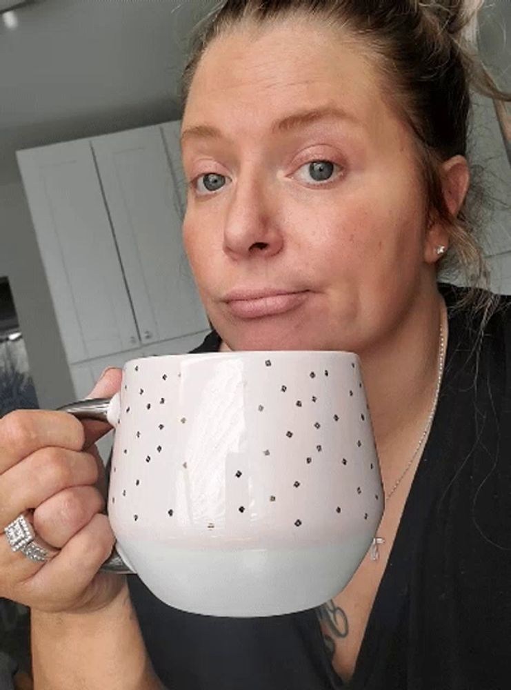 a woman is drinking from a white mug with gold polka dots