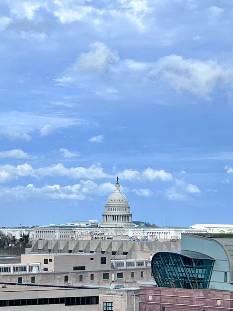 View of US Capitol dome above skyline against sky of blue with a few puffy white clouds 