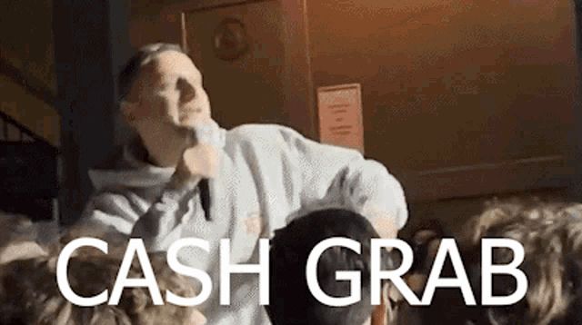 Man yelling into a microphone with the caption “cash grab”
