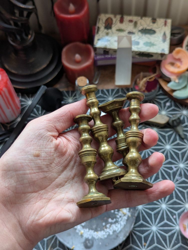 A hand holding four brass candlesticks. They're very small, made for the size of candle that you'd put on a birthday cake.