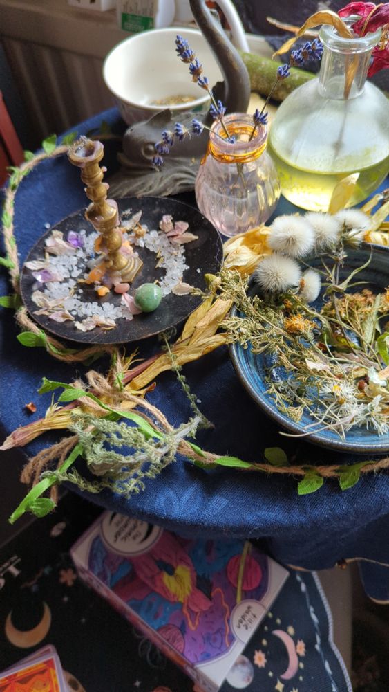 An altar space decorated with dried plants and flowers. A candleholder sits circled by a ring of salt and crystals.