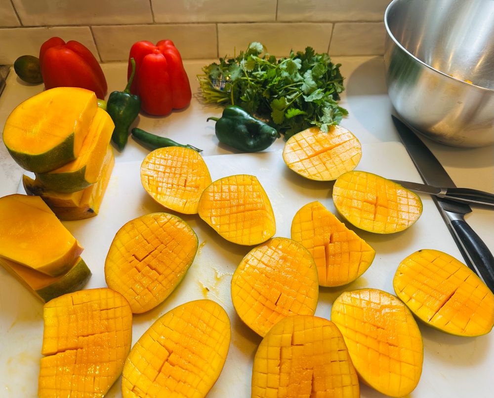 Halved mangos, peppers, cilantro on a cutting board