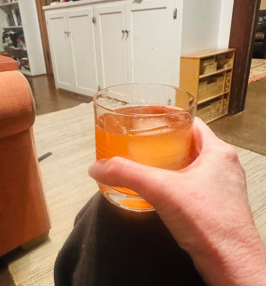 Bright orange pink cocktail over a big ice cube, held in someone's hand 